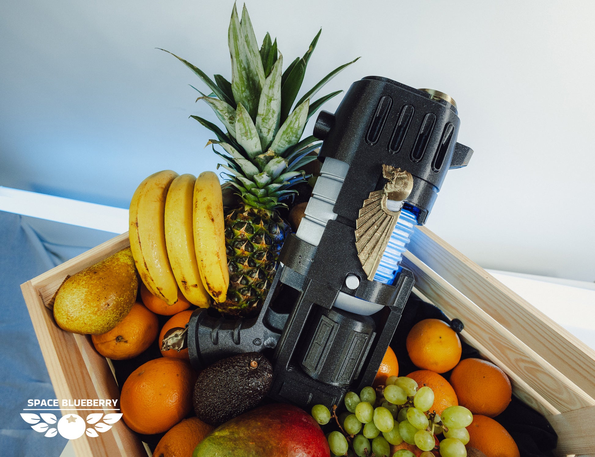Fruit basket with a toy plasma gun on a white background with gold skull and wings.